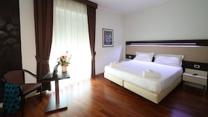 A hotel room with a bed, a desk with a laptop, a chair, a nightstand, and a window with curtains. - Grande Albergo Maugeri (Acireale)