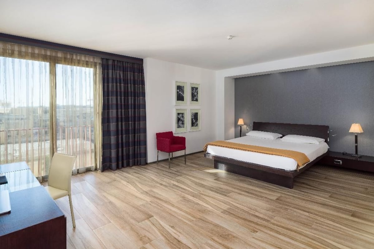 Une chambre d’hôtel avec un lit, un bureau, une chaise, une fenêtre avec des rideaux et une vue sur la ville.