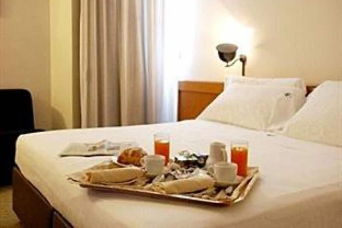 Una habitación de hotel con una cama, una bandeja con alimentos para el desayuno y una mesita de noche con una lámpara.