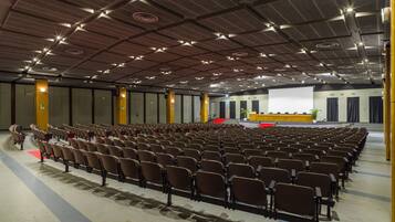 Un ampio auditorium con file di sedie, un palco con un podio e uno schermo grande.