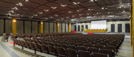 A large auditorium with rows of chairs, a stage with a podium, and a large screen.
