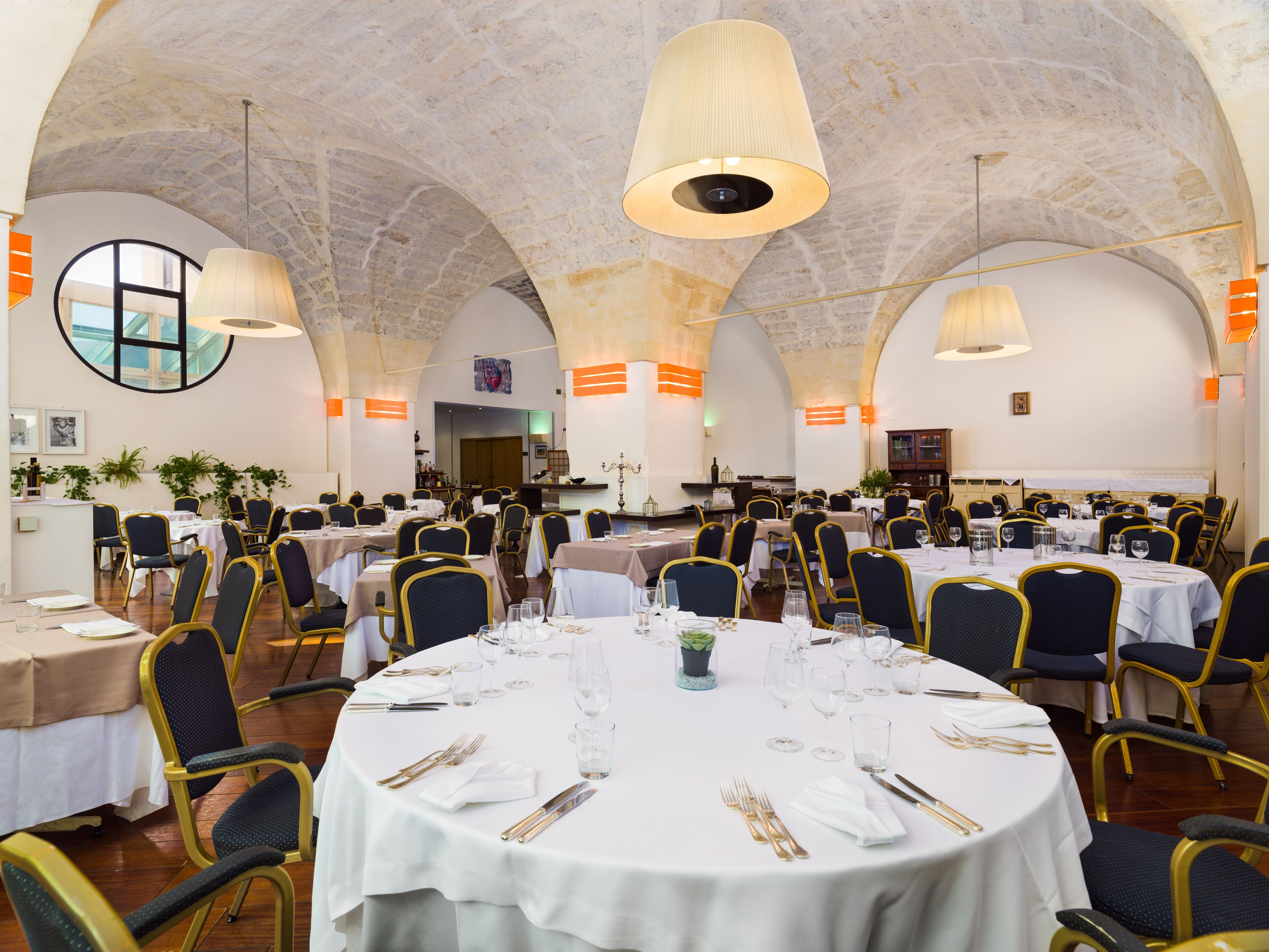 A spacious dining hall with round tables, chairs, and overhead lighting.