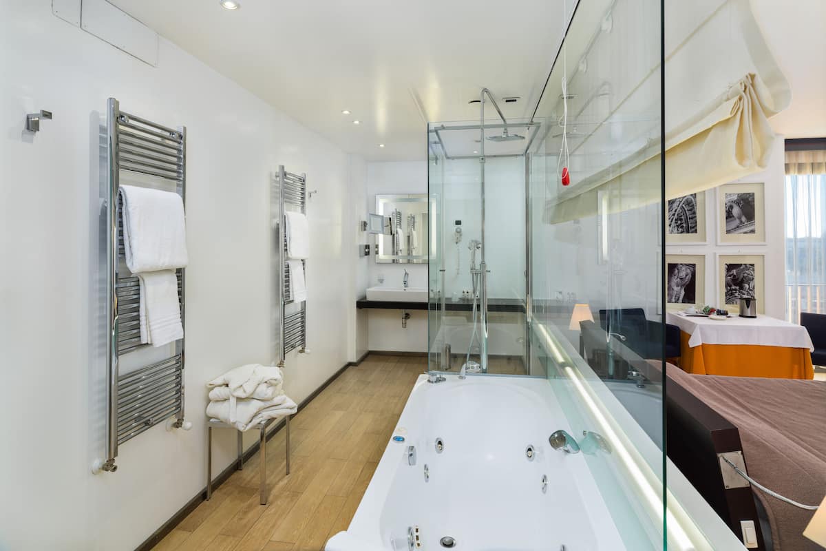 Un baño moderno con ducha envuelta en vidrio, una bañera amplia y un panel de vidrio que separa la zona de la ducha del resto del cuarto.