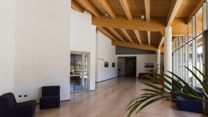A spacious lobby with wooden beams, a glass door leading outside, and a red sofa. - Grand Hotel Tiziano e dei Congressi (Lecce)