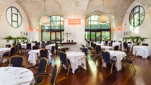 A spacious dining hall with high ceilings and large windows, featuring round tables and chairs, and a central chandelier. - Grand Hotel Tiziano e dei Congressi (Lecce)