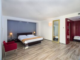 Una habitación de hotel moderna con una cama grande, lámparas de noche, una silla roja y un espejo en la pared.