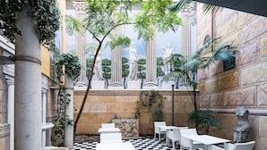Une cour intérieure avec des tables et des chaises blanches, un sol à carreaux et des colonnes de style classique.