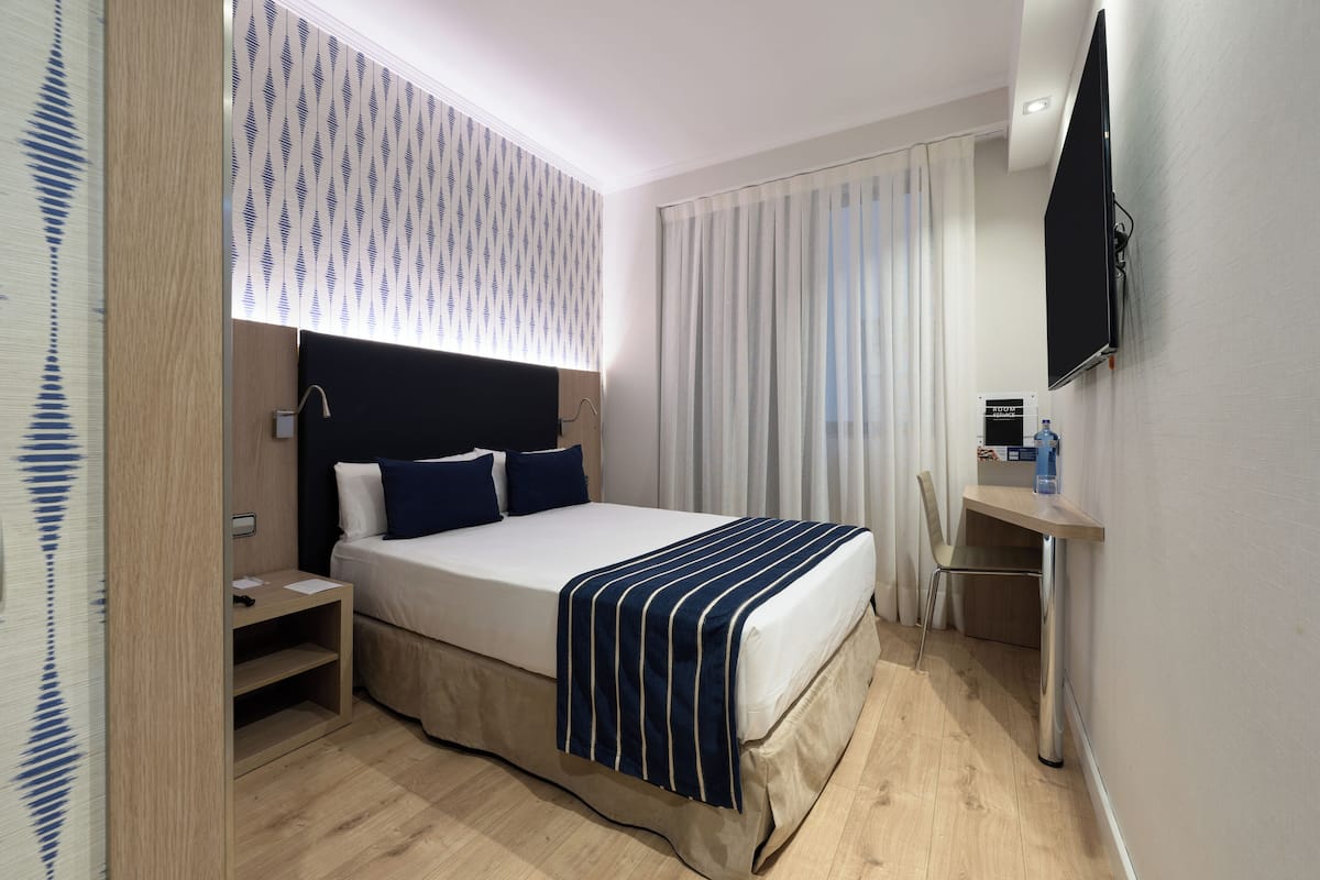 Ein modernes Hotelzimmer mit Bett, Nachttisch, Fernseher und Schreibtisch mit Stuhl.
