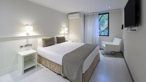 Une chambre d’hôtel moderne avec un grand lit, des lampes de chevet, un téléviseur à écran plat, une fenêtre avec des rideaux et une chaise blanche.