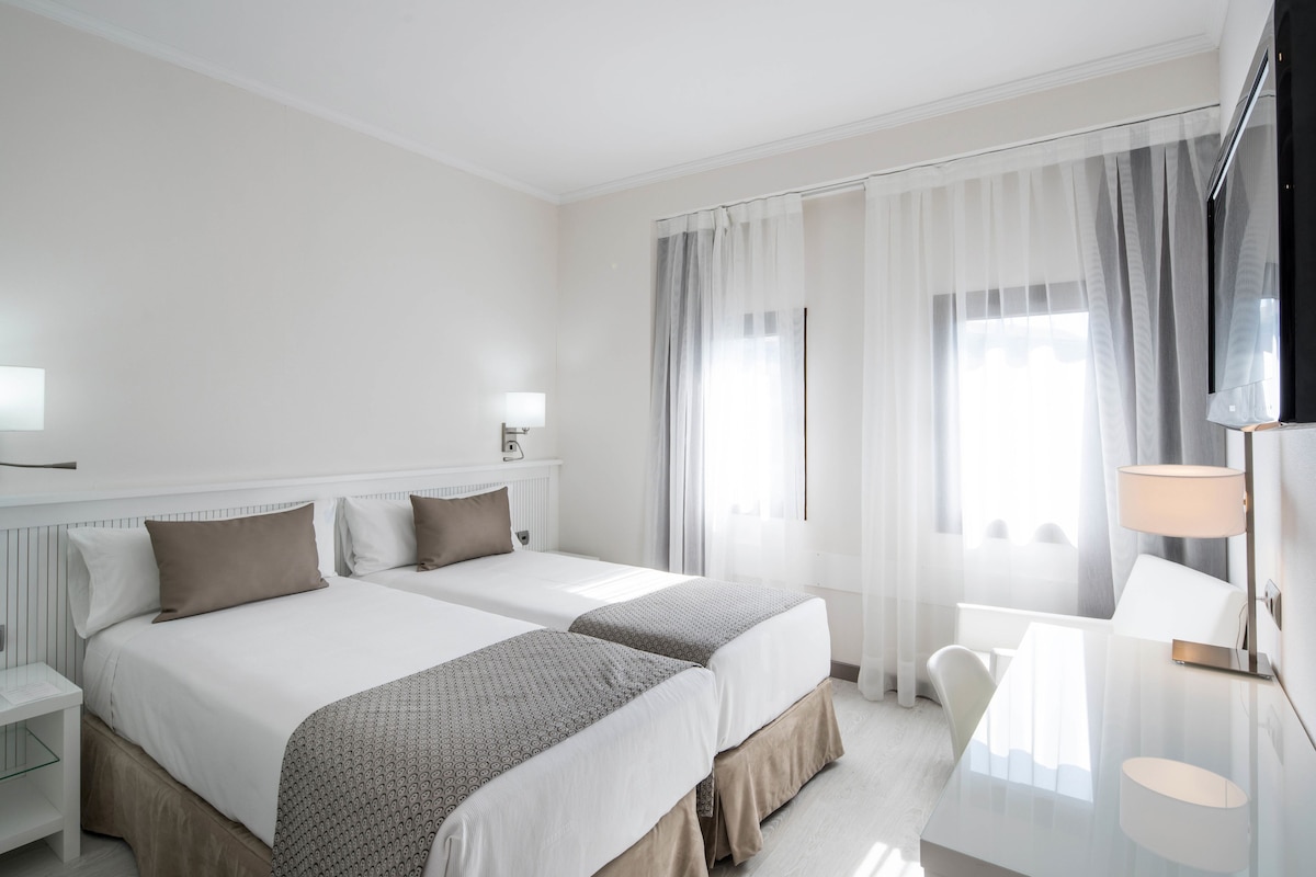 A hotel room with two beds, a desk, and a chair.