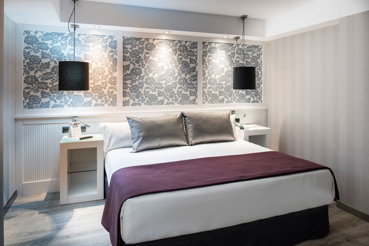 Ein modernes Hotelzimmer mit einem großen Bett, einem Nachttisch, einem Wand-TV und einer dekorativen Wandverkleidung.