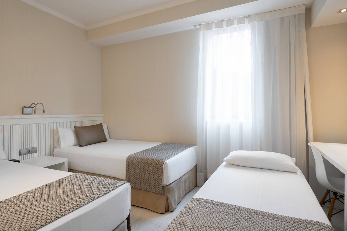 Ein Hotelzimmer mit zwei Betten, einem Schreibtisch und einem Fenster mit Vorhängen.