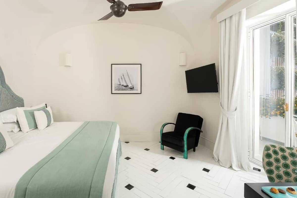 A bedroom with a bed, a chair, a TV, and a window with curtains.