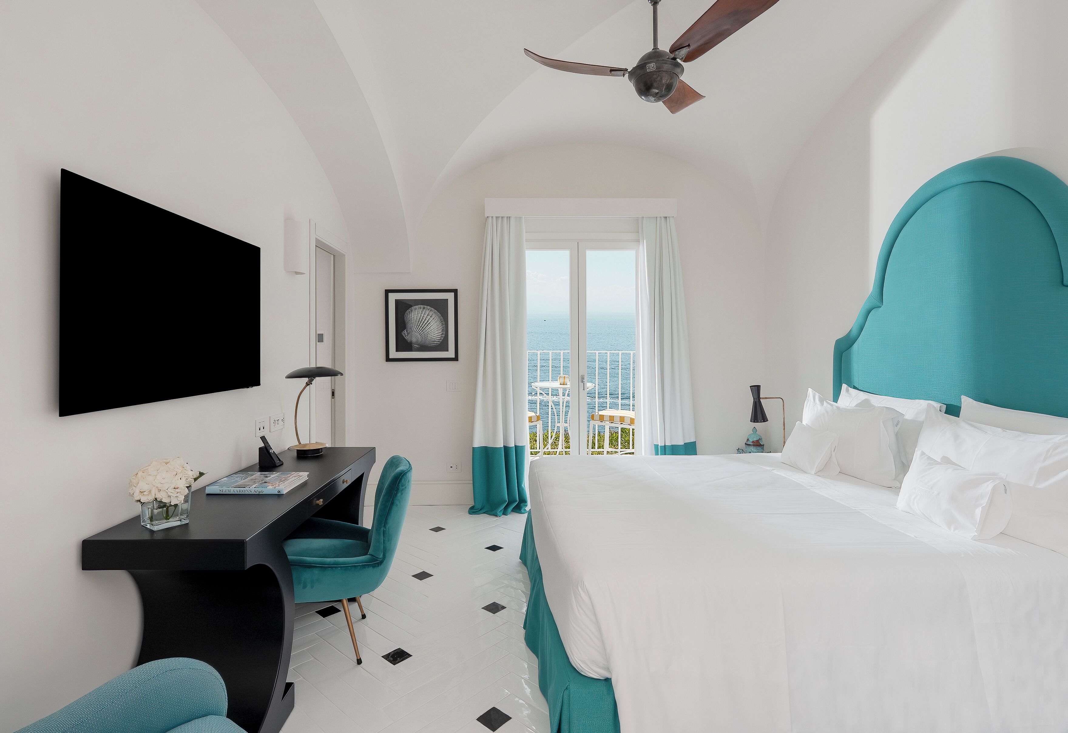 Una camera d'albergo con un letto, una scrivania, una sedia, una TV e vista sul mare.