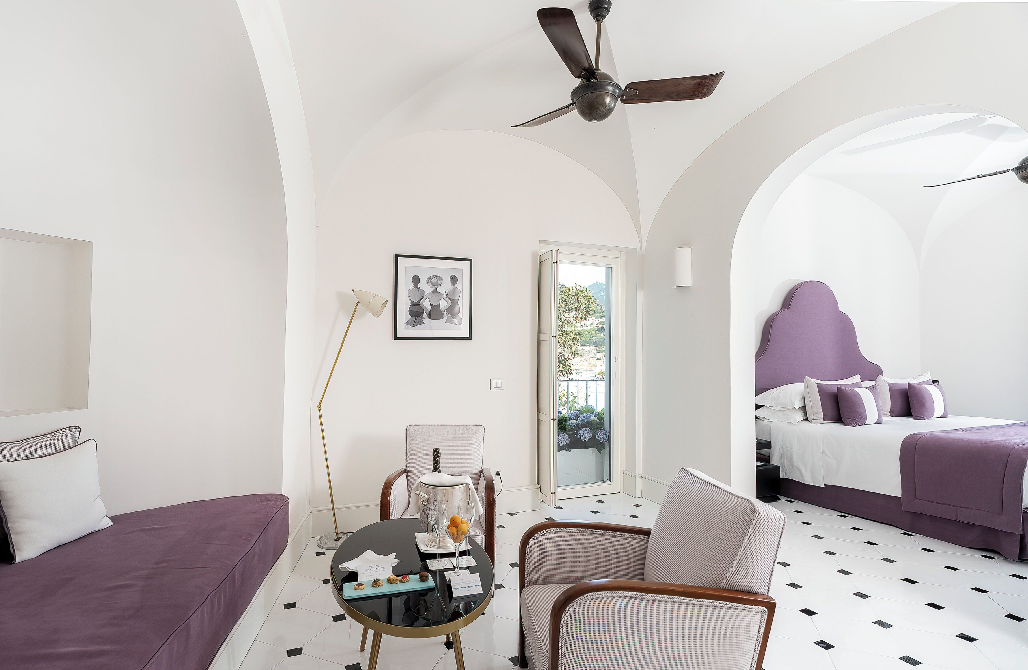 Una camera d'albergo con un letto, una poltrona, un tavolo da pranzo e una ventola a soffitto.