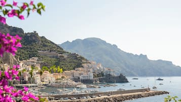 A coastal town with buildings on a hillside, a marina with boats, and a rocky breakwater.