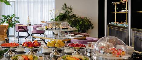 Ein reichhaltiges Buffet mit verschiedenen Früchten und Speisen, ein Sitzbereich mit Stühlen und eine Zierpflanze.
