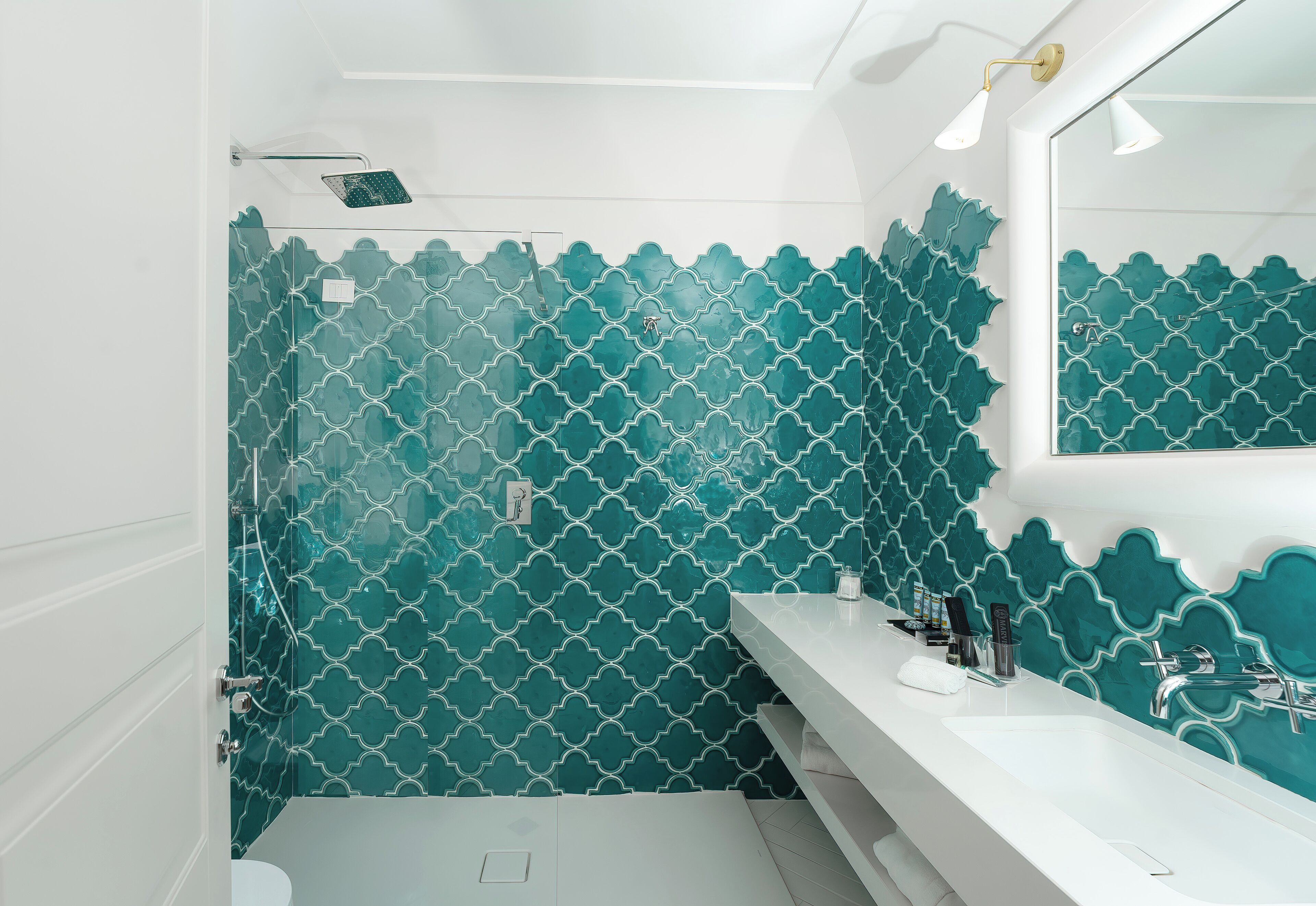 Un bagno con un lavandino bianco, uno specchio e una doccia con piastrelle a motivi color acquamarina.