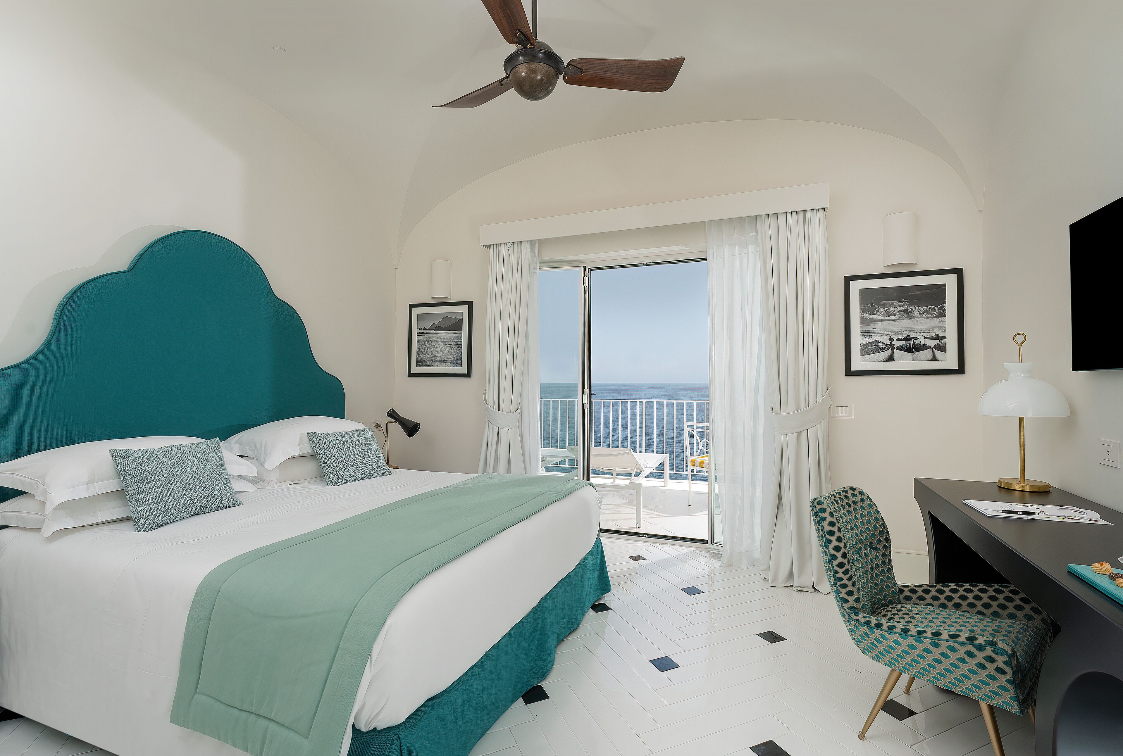 Quarto de hotel com cama, escrivaninha, cadeira e varanda com vista para o mar.
