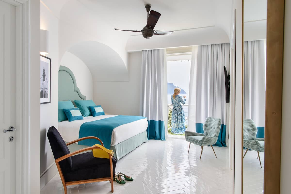 A hotel room with a bed, a chair, a ceiling fan, and a view of the outdoors.