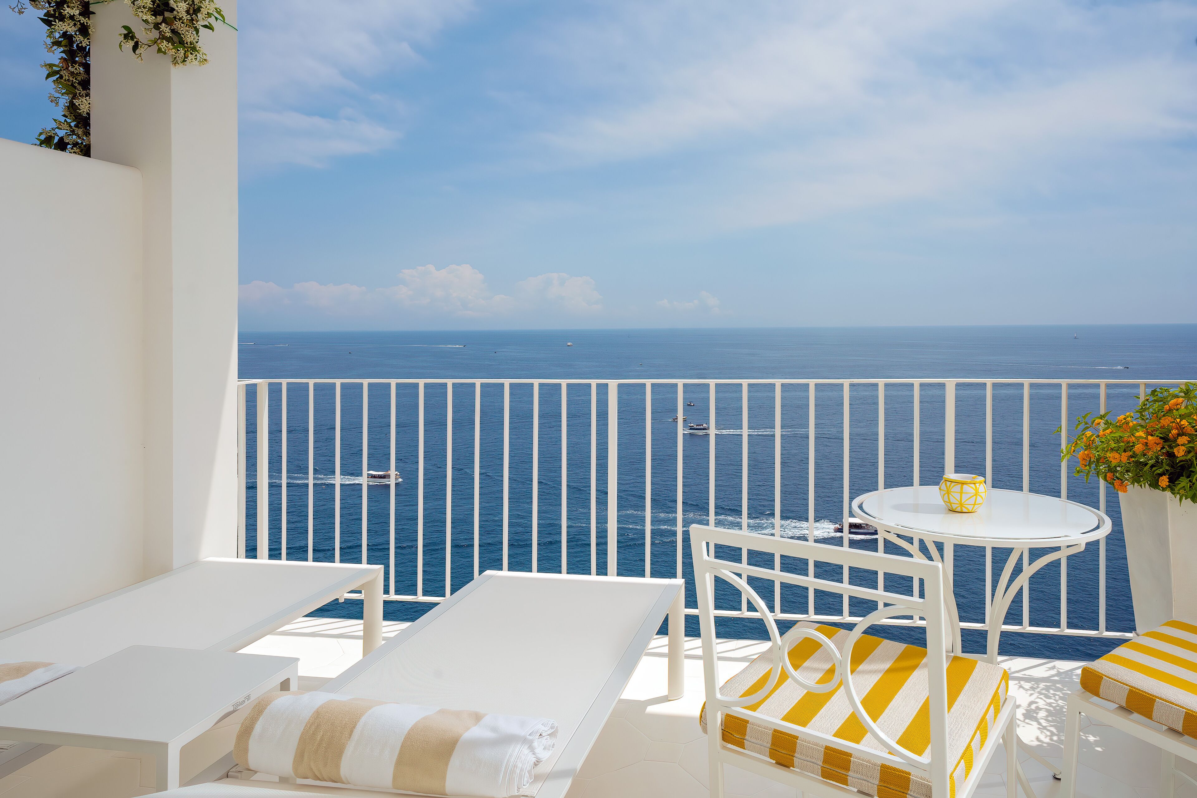 A balcony with white furniture, a small table with a yellow bowl, and a view of the sea.