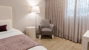 Una habitación de hotel con cama, una silla, una lámpara y un ventanal con cortinas.