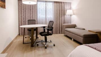 Habitació d'hotel amb una taula rodona, dues cadires d'oficina, un sofà, un llit i una làmpada.