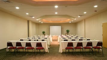 A conference room with multiple tables and chairs, a projector screen, and a carpeted floor.