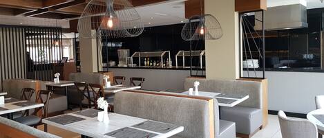 Ein modernes Restaurantambiente mit Sitzecken, Pendelleuchten und einer Bar im Hintergrund.