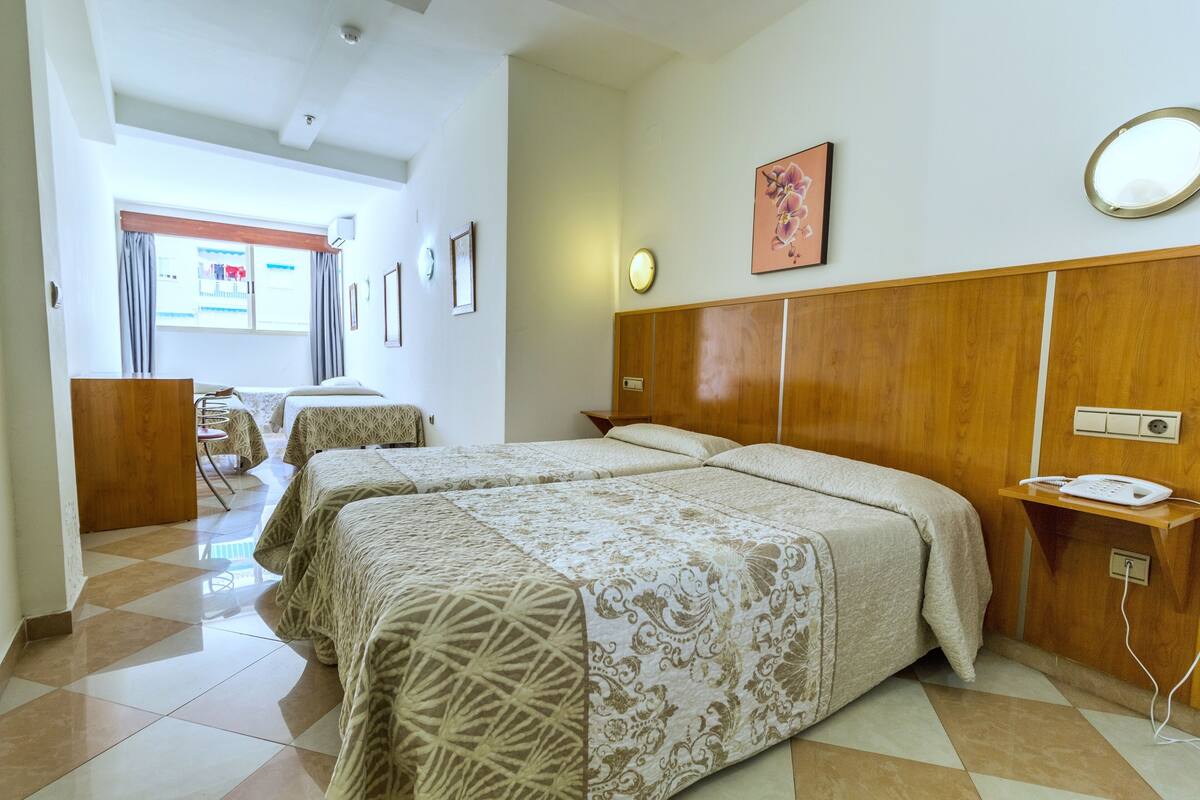 Een hotelkamer met twee bedden, een houten hoofdbord, een tafeltje, een stoel en een raam met gordijnen.