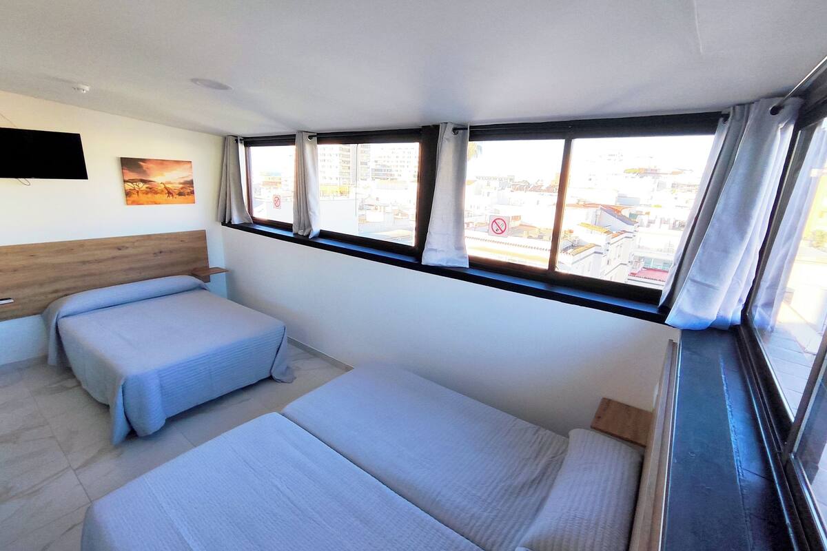 Een hotelkamer met twee bedden, een houten hoofdeinde, een flatscreen televisie en een raam met gordijnen.
