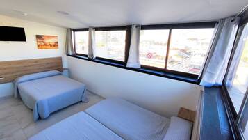 Habitación de hotel con dos camas, cabecera de madera, televisor de pantalla plana y ventana con cortinas.