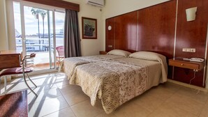 Een hotelkamer met een bed, een bureau, een stoel, een raam met uitzicht en een nachtkastje met telefoon.
