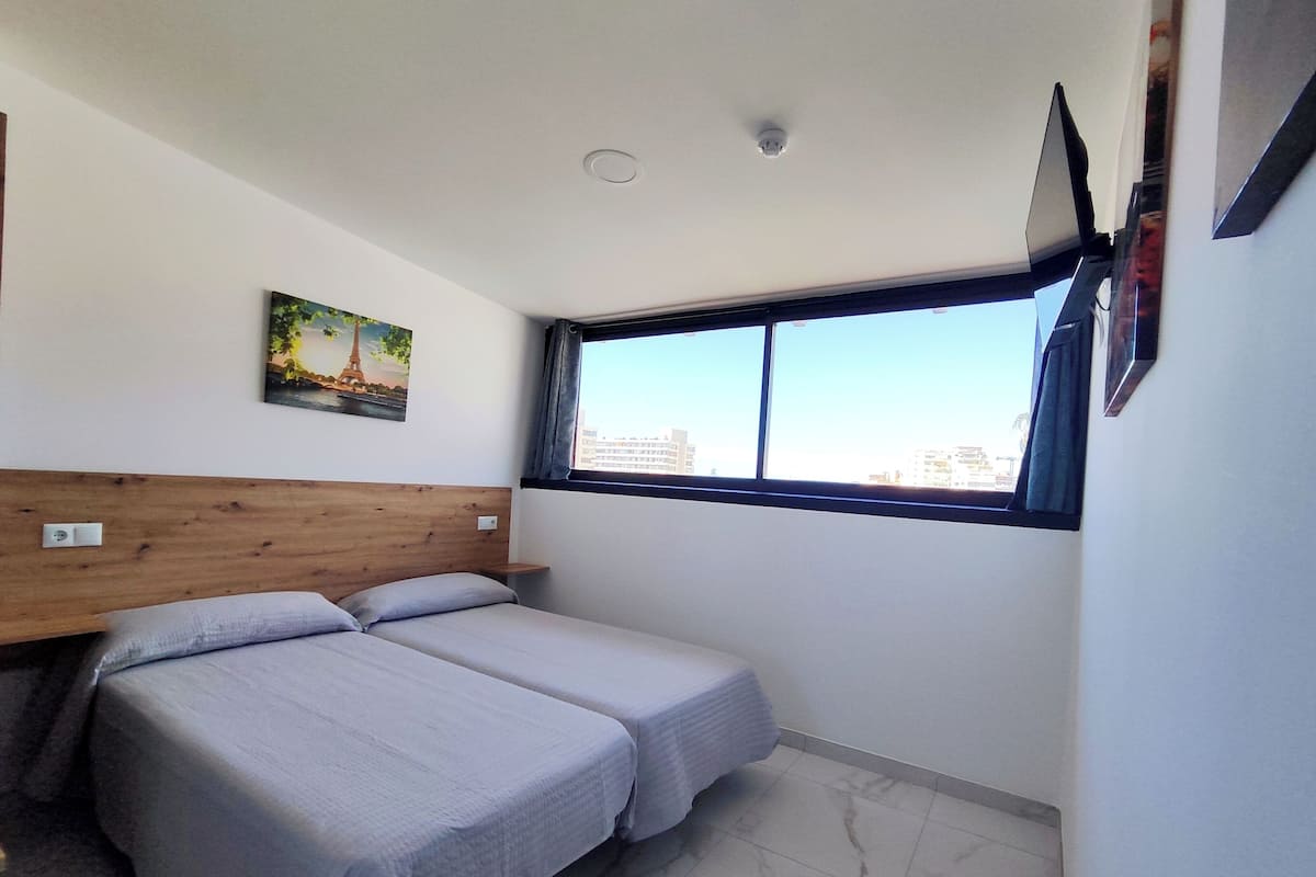 Een hotelkamer met twee bedden, een houten hoofdeinde, een schilderij, een raam met uitzicht op de stad en een tv aan de muur.