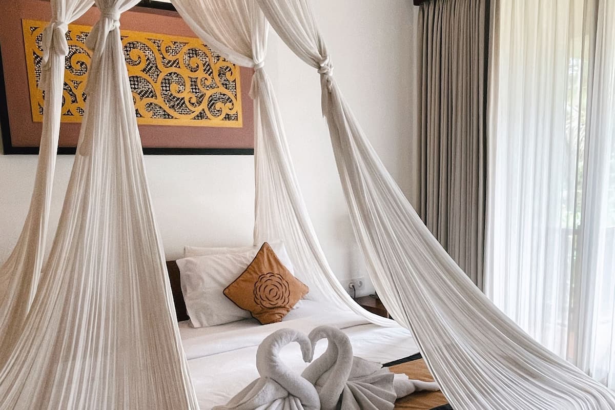 Un dormitorio con cama de dosel, cabecera de madera, almohada decorativa y una obra de arte en la pared.