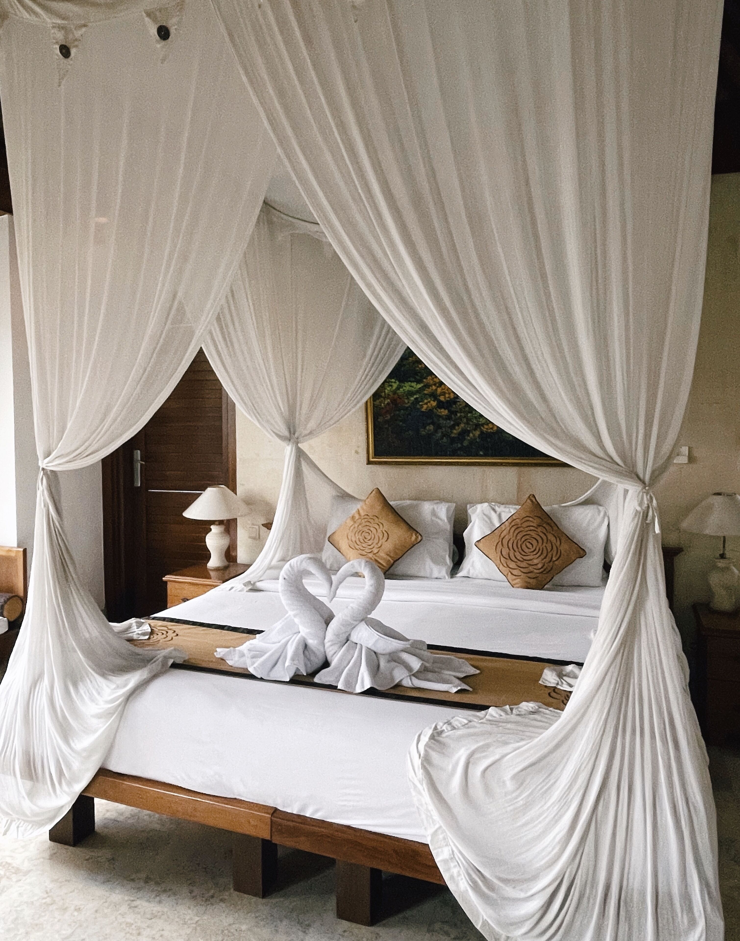 Una cama con dosel y cuatro columnas, con una decoración de cisne, cabecera de madera y dos almohadas con diseños florales.