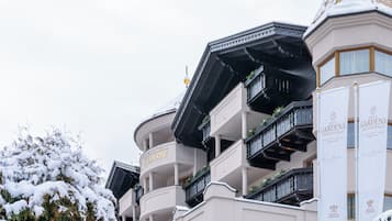 Un hotel de varios pisos con balcones, un árbol cubierto de nieve y señalización para Hotel Gardena y Relais & Chateaux.