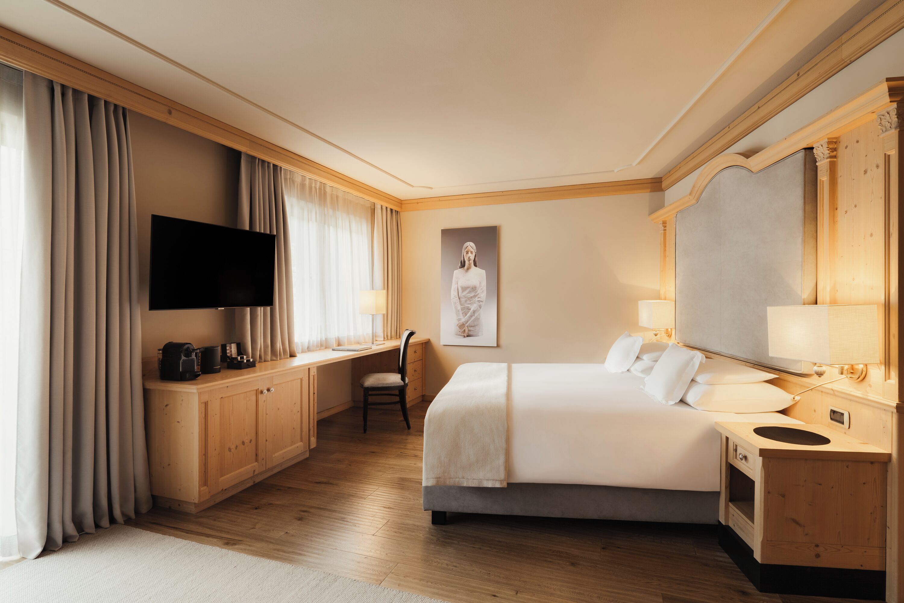 Ein Hotelzimmer mit Bett, Schreibtisch, Stuhl, Fernseher und Kunstwerken.