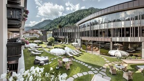 Un pati d'hotel modern amb seients exteriors, un edifici de vidre i un paisatge de muntanyes al fons.