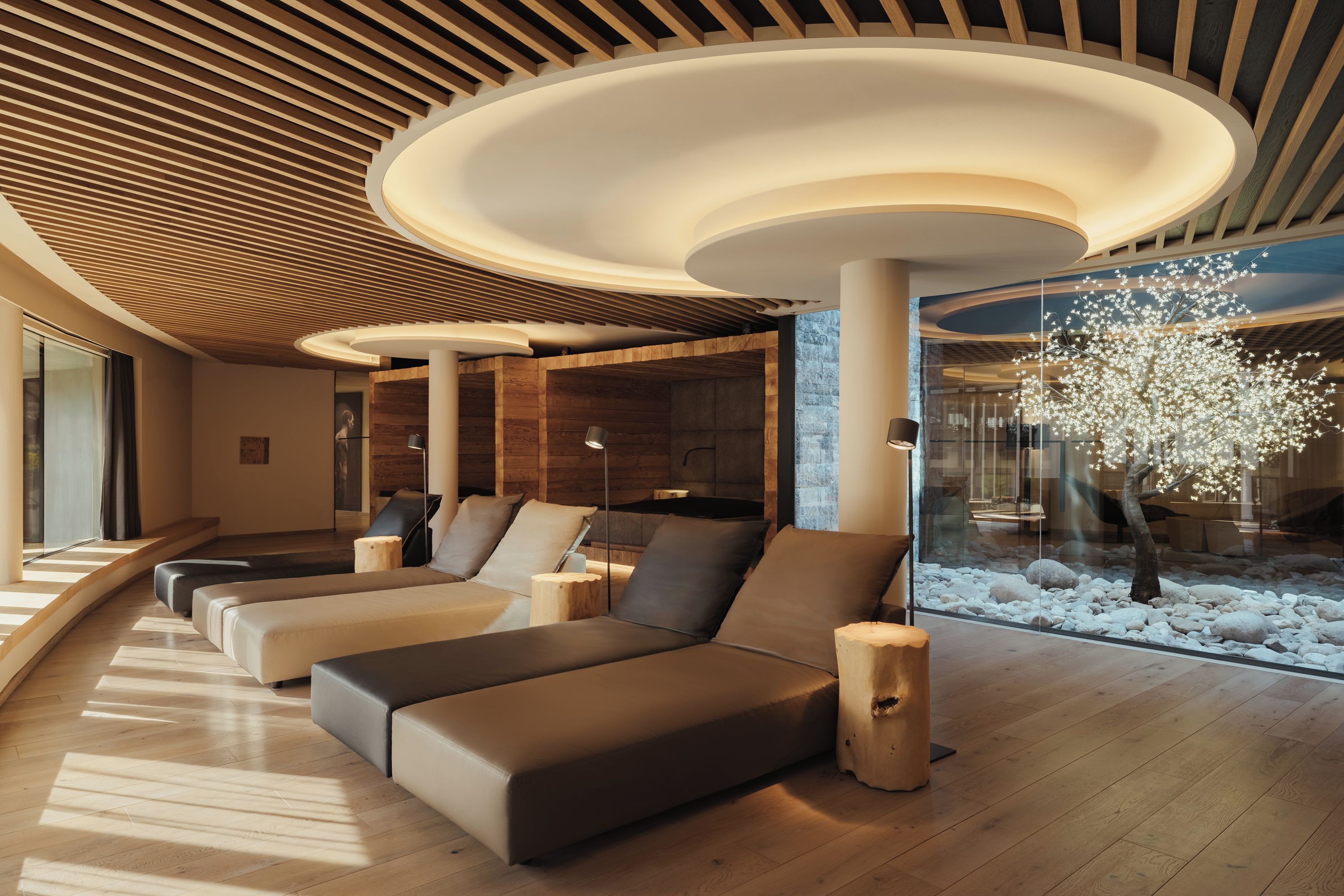 Un área de descanso moderna con techo de madera, una gran escultura de árbol y una zona de asientos con cojines.