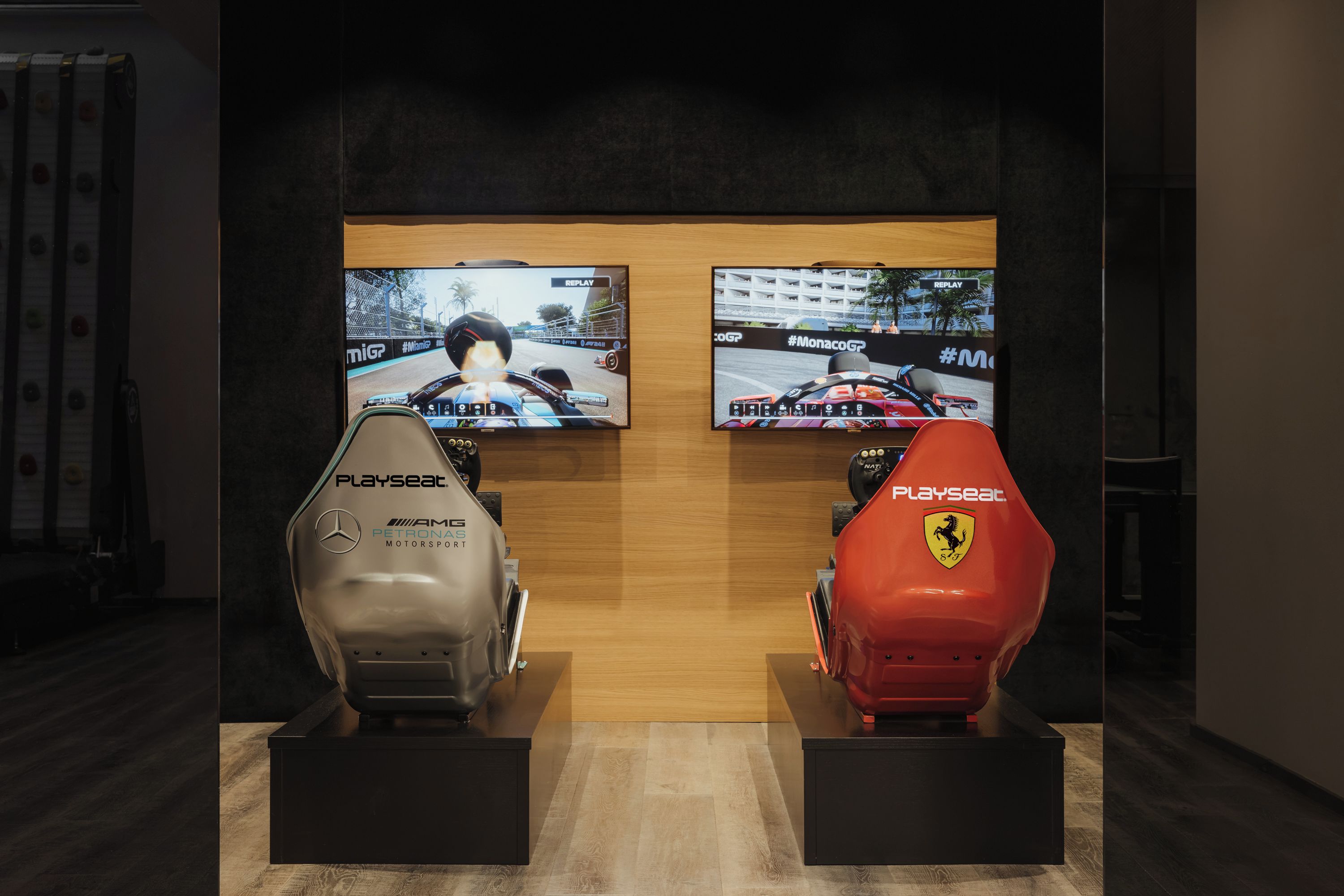 Deux simulateurs de course arborant la marque « Playseat », un mur en bois et deux écrans affichant un jeu de course.