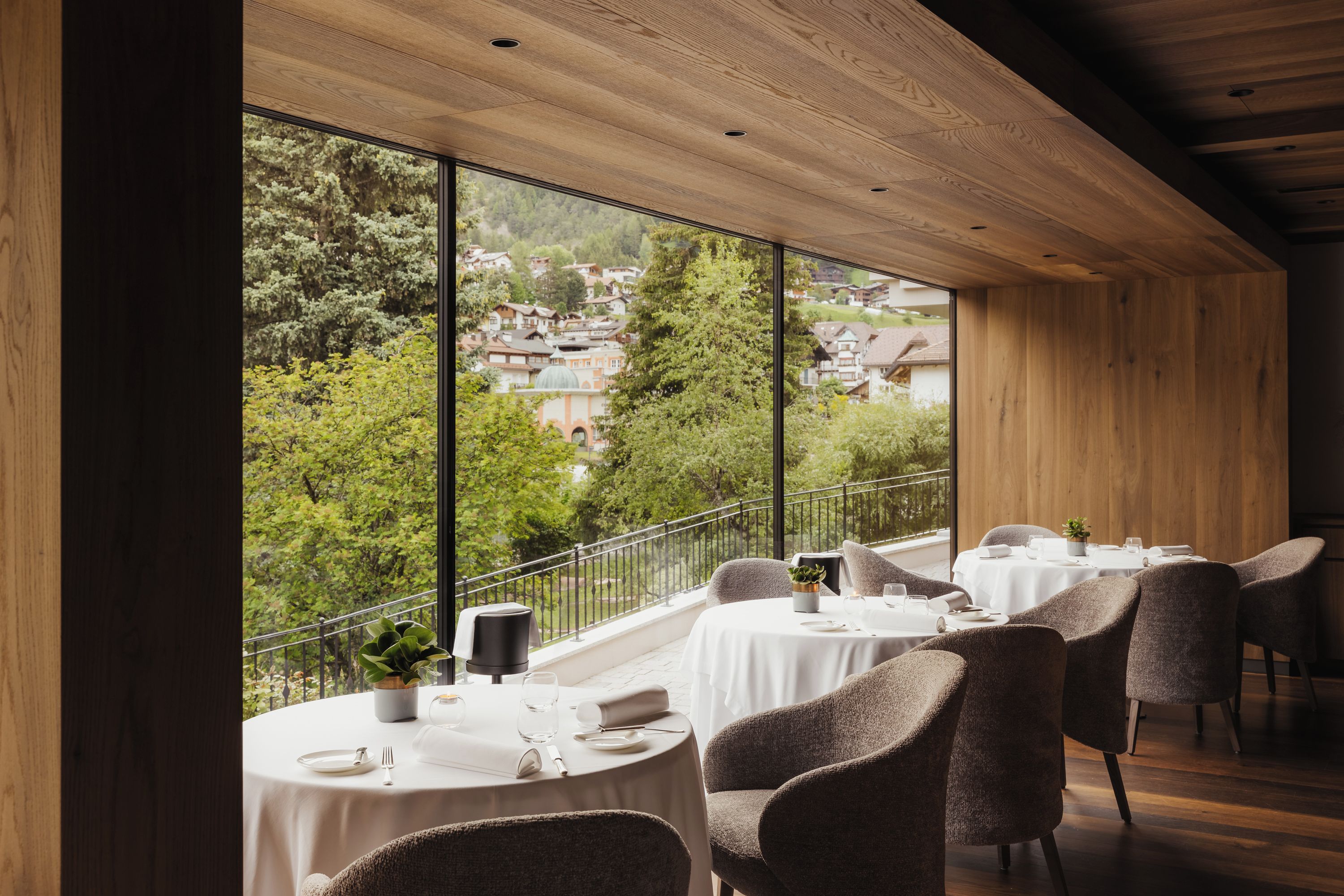 Un restaurant amb taules rodones, cadires i vistes a una vila a través de grans finestres.