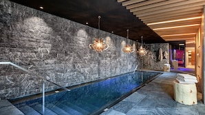 Un espace de bien-être doté d’un mur en pierre, d’une piscine et de poutres en bois au plafond.