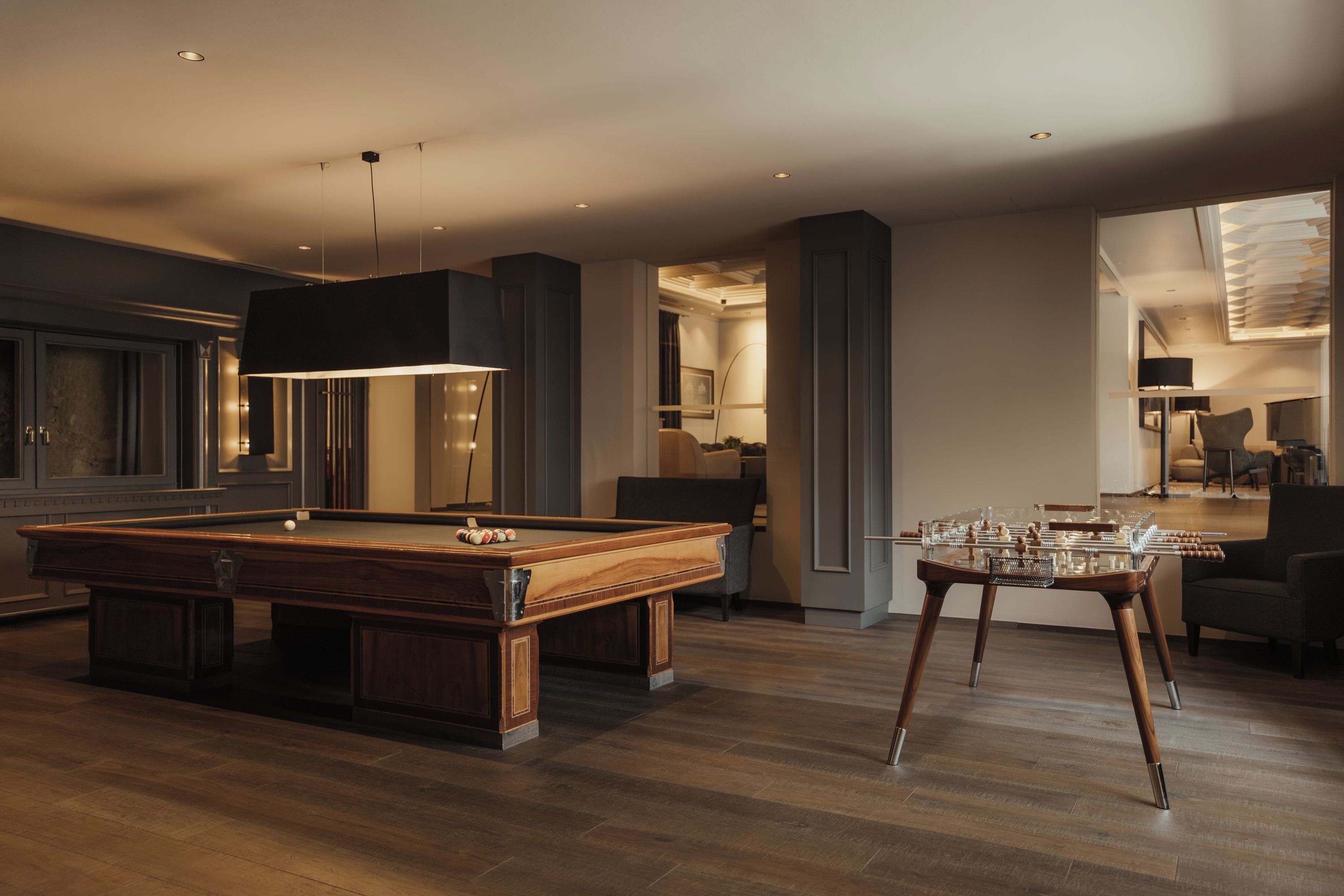 A modern indoor setting with a pool table, a foosball table, and a bar area.