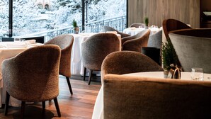 Un restaurant avec des tables et des chaises rondes, une vue sur des arbres et des bâtiments couverts de neige, et des murs recouverts de lambris en bois.