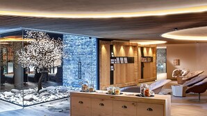 Un intérieur moderne avec un comptoir d’accueil en bois, un mur de verre orné d’un arbre en fleurs de cerisier et un espace détente avec des fauteuils confortables.