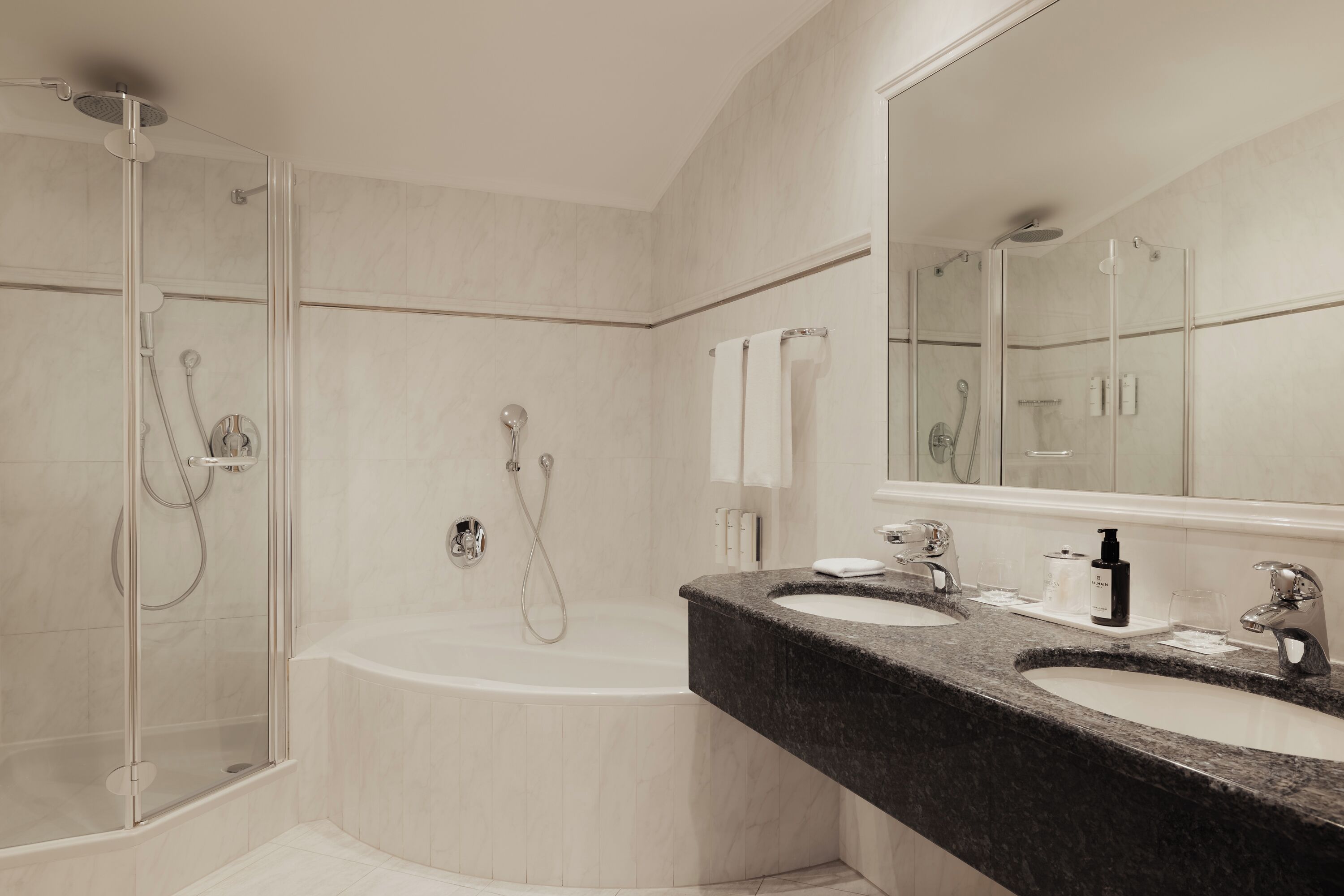 Un baño moderno con ducha envuelta en vidrio, una bañera independiente y un mostrador de granito con dos lavamanos.