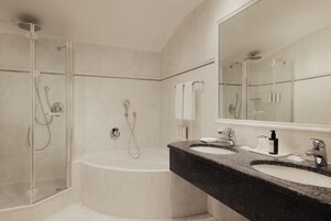 Un baño moderno con ducha envuelta en vidrio, una bañera independiente y un mostrador de granito con dos lavamanos.