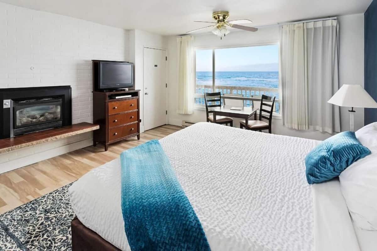 Une chambre d’hôtel avec un lit, une télévision, une cheminée, un balcon avec une table et des chaises, et une vue sur l’océan.