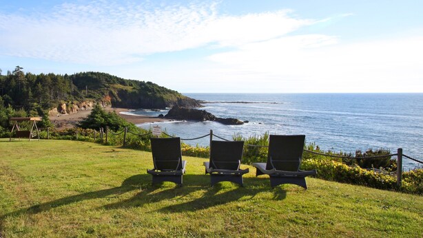 A grassy area with three lounge chairs facing a coastal view.